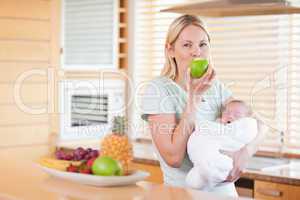 Woman enjoying an apple with her baby on her arms