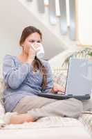 Portrait of a woman using a laptop while drinking a cup of tea