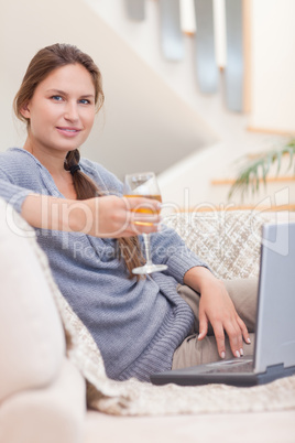 Portrait of a woman having a glass of wine while using her lapto