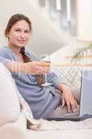 Portrait of a woman having a glass of wine while using her lapto