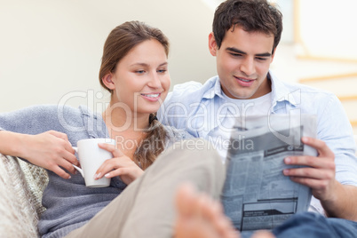Couple reading the news while lying on a sofa