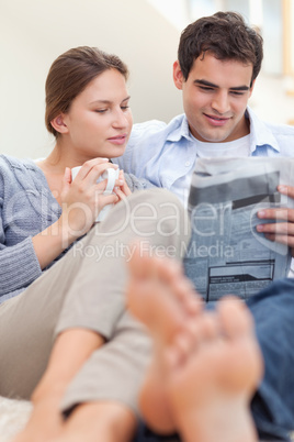 Couple reading a newspaper while lying on a sofa