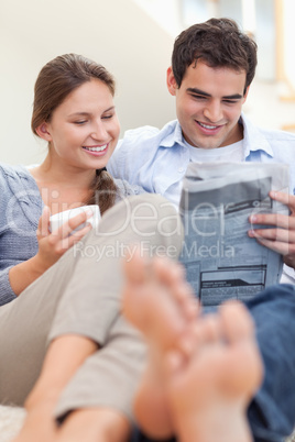 Couple reading a newspaper while lying on a couch