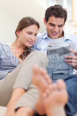 Portrait of a couple reading a newspaper while lying on a couch