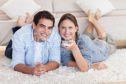 Cute couple watching TV while lying on a carpet