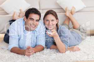 Cute couple watching TV while lying on a carpet
