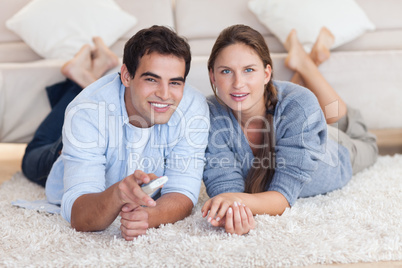 Lovely couple watching TV while lying on a carpet