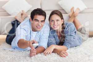 Smiling couple watching TV while lying on a carpet