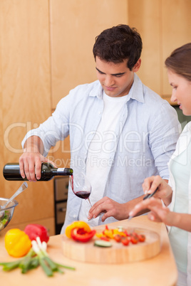 Portrait of a man pouring a glass of wine while his wife is cook