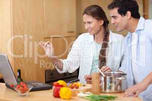 Smiling couple using a laptop to cook