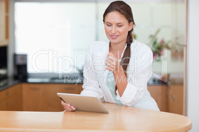 Young woman using a tablet computer while drinking coffee