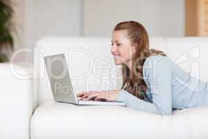 Cheerful smiling woman on the sofa typing on her laptop