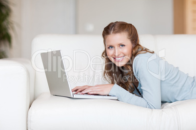 Cheerful smiling woman on the couch typing on her laptop