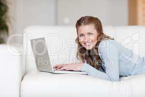 Cheerful smiling woman on the couch typing on her laptop