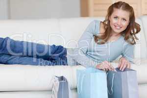 Smiling woman lying on the sofa next to her shopping