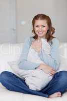 Smiling female sitting on the sofa hugging a pillow