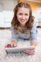 Smiling woman with tablet laying on the carpet