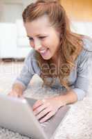 Smiling woman lying on the carpet with her laptop