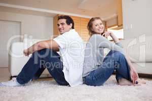 Side view of young couple sitting on the floor back-to-back