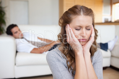 Woman having headache while man lying on sofa behind her
