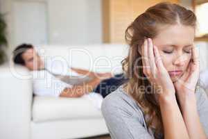 Woman experiencing headache with man on the sofa behind her