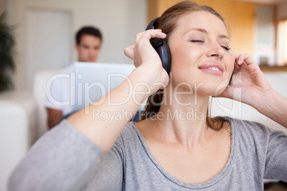 Woman listening to music with man sitting behind her on the sofa