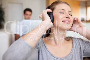 Woman listening to music with man sitting behind her on the sofa