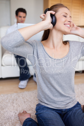 Woman with earphones on the carpet and man behind her on the sof