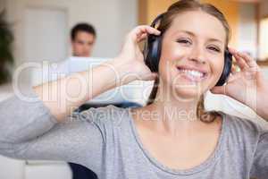 Woman with headphones on with man sitting behind her on the sofa