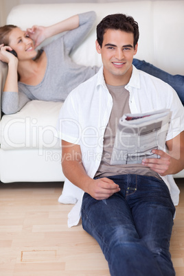 Man leaning against the sofa with newspaper while his girlfriend