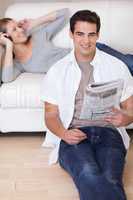Man leaning against the sofa with newspaper while his girlfriend