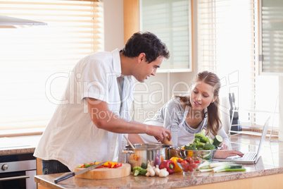 Couple using laptop to look up recipe for their meal