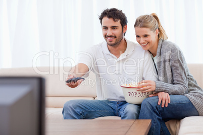 Smiling couple watching TV while eating popcorn