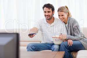 Smiling couple watching TV while eating popcorn