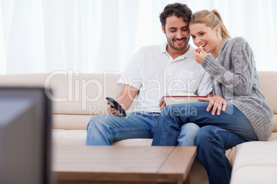 Charming couple watching TV while eating popcorn