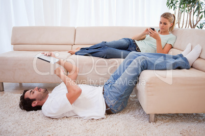 Woman using her phone while her husband is using a tablet comput