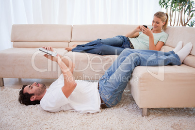 Woman using her phone while her fiance is using a tablet compute