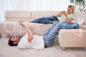 Woman using her phone while her fiance is using a tablet compute