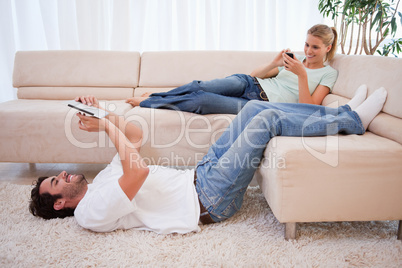 Woman using her phone while her boyfriend is using a tablet comp