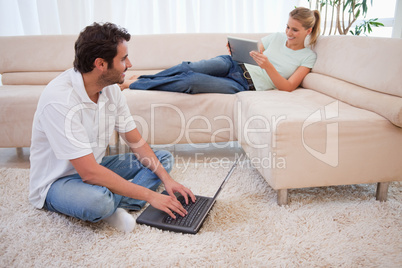 Woman using a tablet computer while her fiance is using a laptop