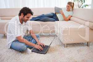 Woman using a tablet computer while her boyfriend is using a lap