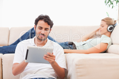 Man using a tablet computer while his girlfriend is listening to