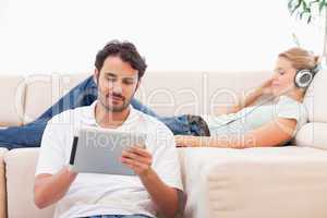 Man using a tablet computer while his girlfriend is listening to
