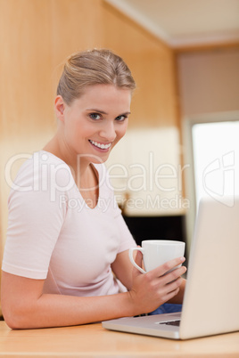 Portrait of a woman using a laptop while drinking a cup of a cof