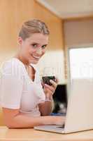 Portrait of a woman using a laptop while drinking red wine