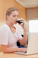 Portrait of a young woman using a laptop while drinking red wine