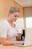Portrait of a woman using a laptop while drinking milk