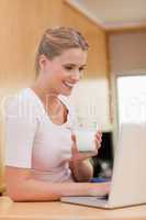 Portrait of a young woman using a laptop while drinking milk
