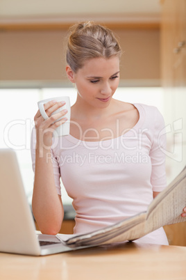 Portrait of a woman reading a newspaper while having tea