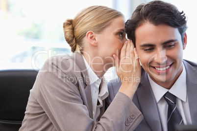 Young businesswoman whispering something to her colleague